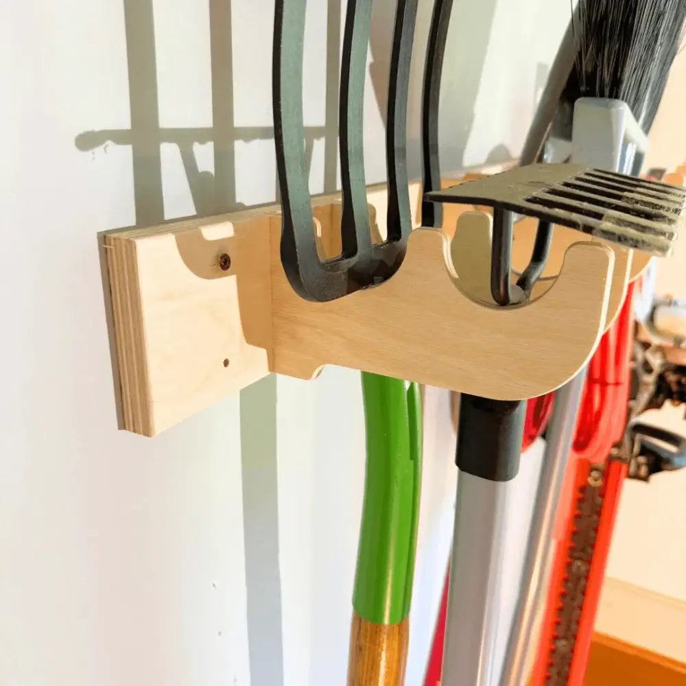 Birch plywood heavy duty garage wall tool rack in light wood holding black metal rakes and brooms