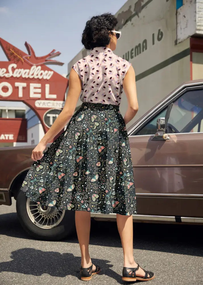 A woman wearing a vintage hedgehog print cotton pink sleeveless blouse with black polka dots and a dark green skirt