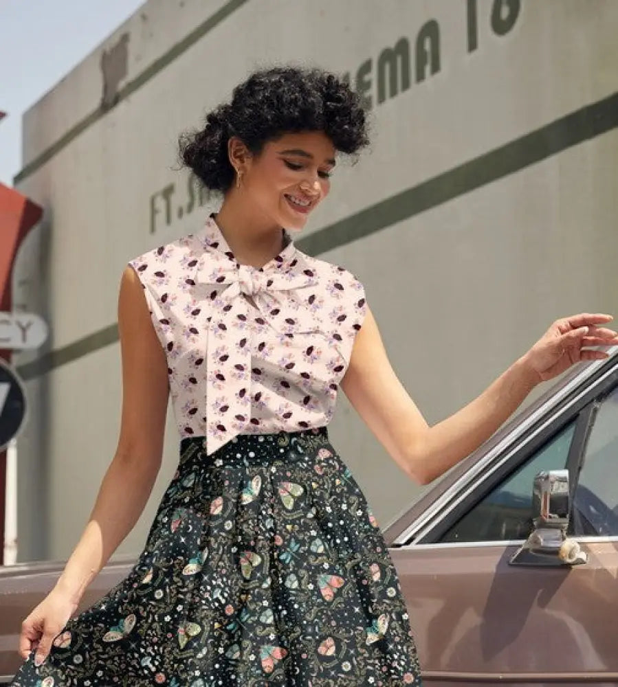 A woman wears a sleeveless vintage hedgeghog print cotton bow blouse with a white base and black butterfly print
