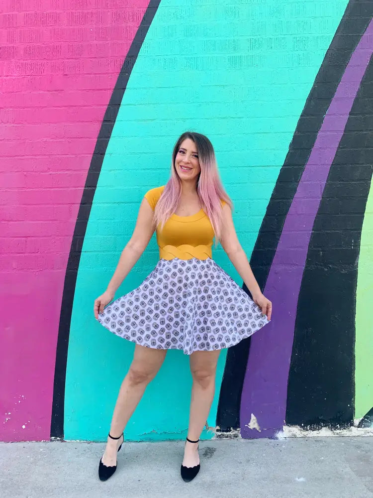 A woman wearing a retro hedgehog print cotton skater skirt in white with purple geometric patterns and a yellow top