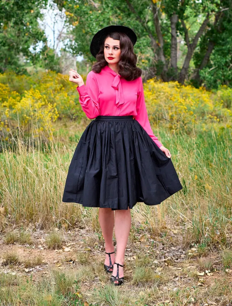 A woman wearing a helen pink bow tie retro long sleeve blouse paired with a black full skirted dress