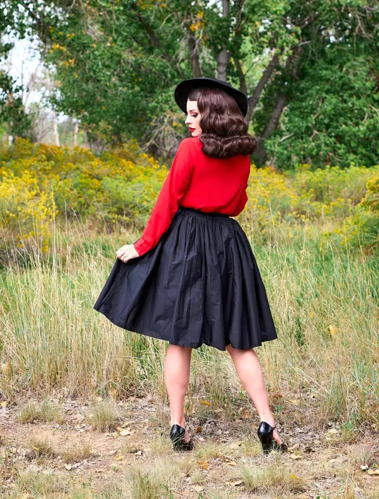 A woman wearing helen retro red bow tie long sleeve plus size blouse paired with black skirt and hat