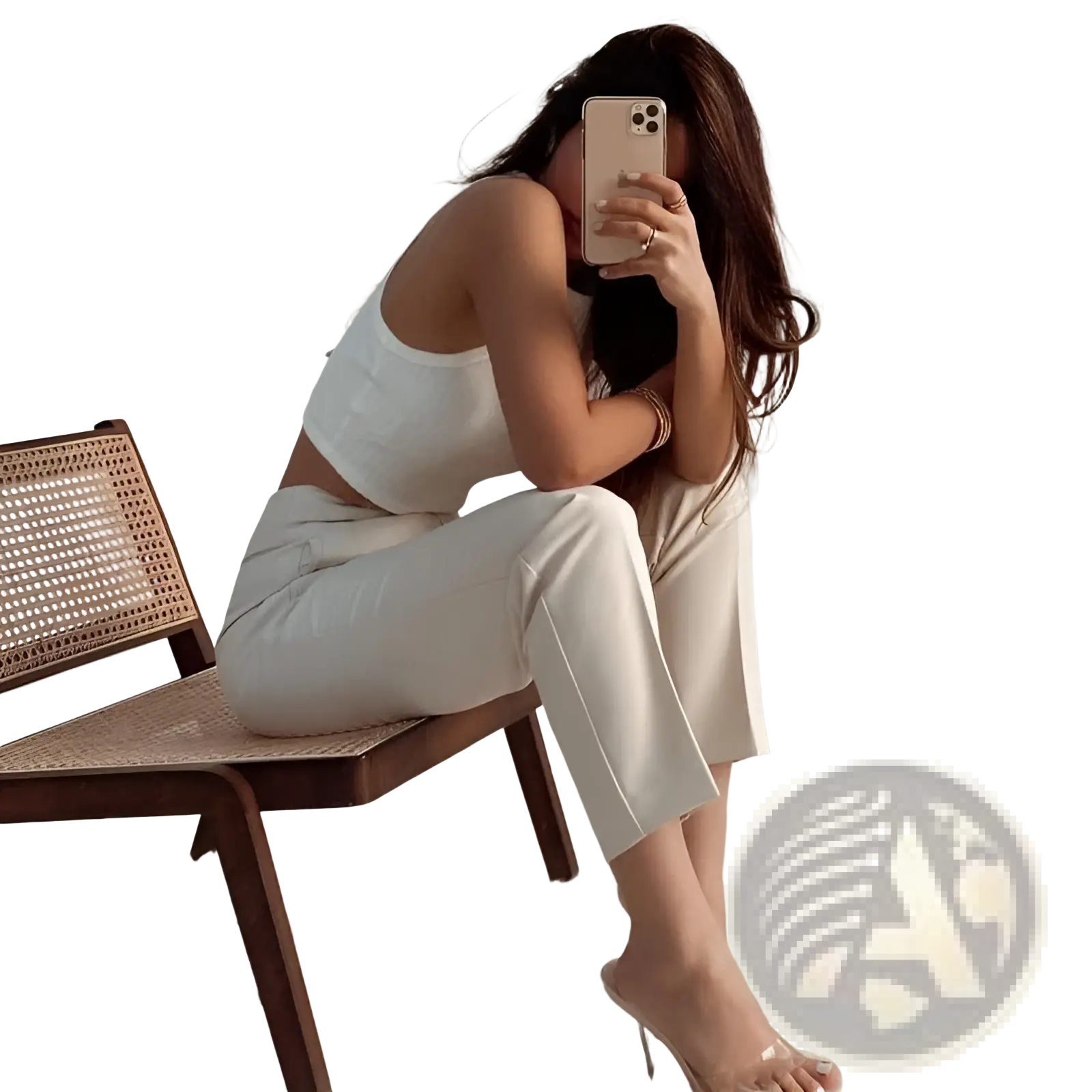 A woman wearing white high waist pleated straight leg trousers and a crop top seated on a wooden cane chair