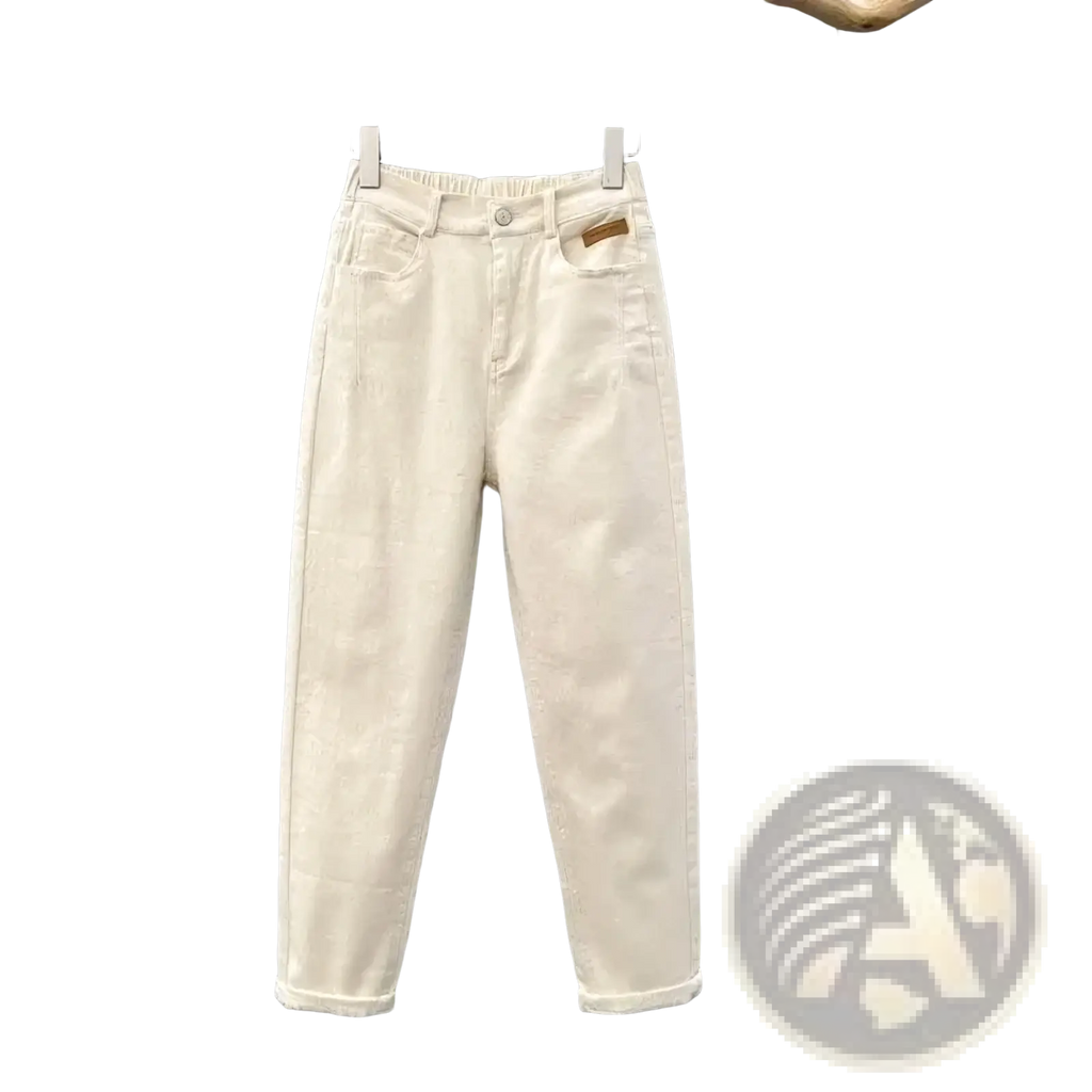 Cream-colored high waisted loose denim carrot pants with relaxed fit and rolled cuffs hanging on wooden hanger