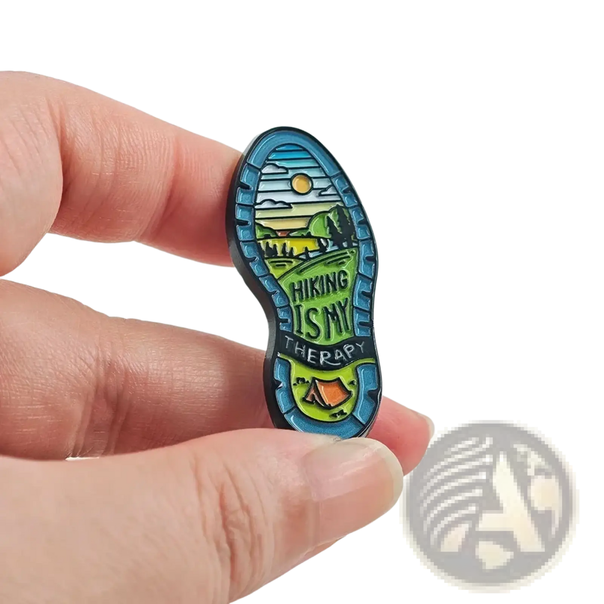 A colorful enamel hiking boot sole pin featuring a scenic mountain and tree landscape under a sunlit sky