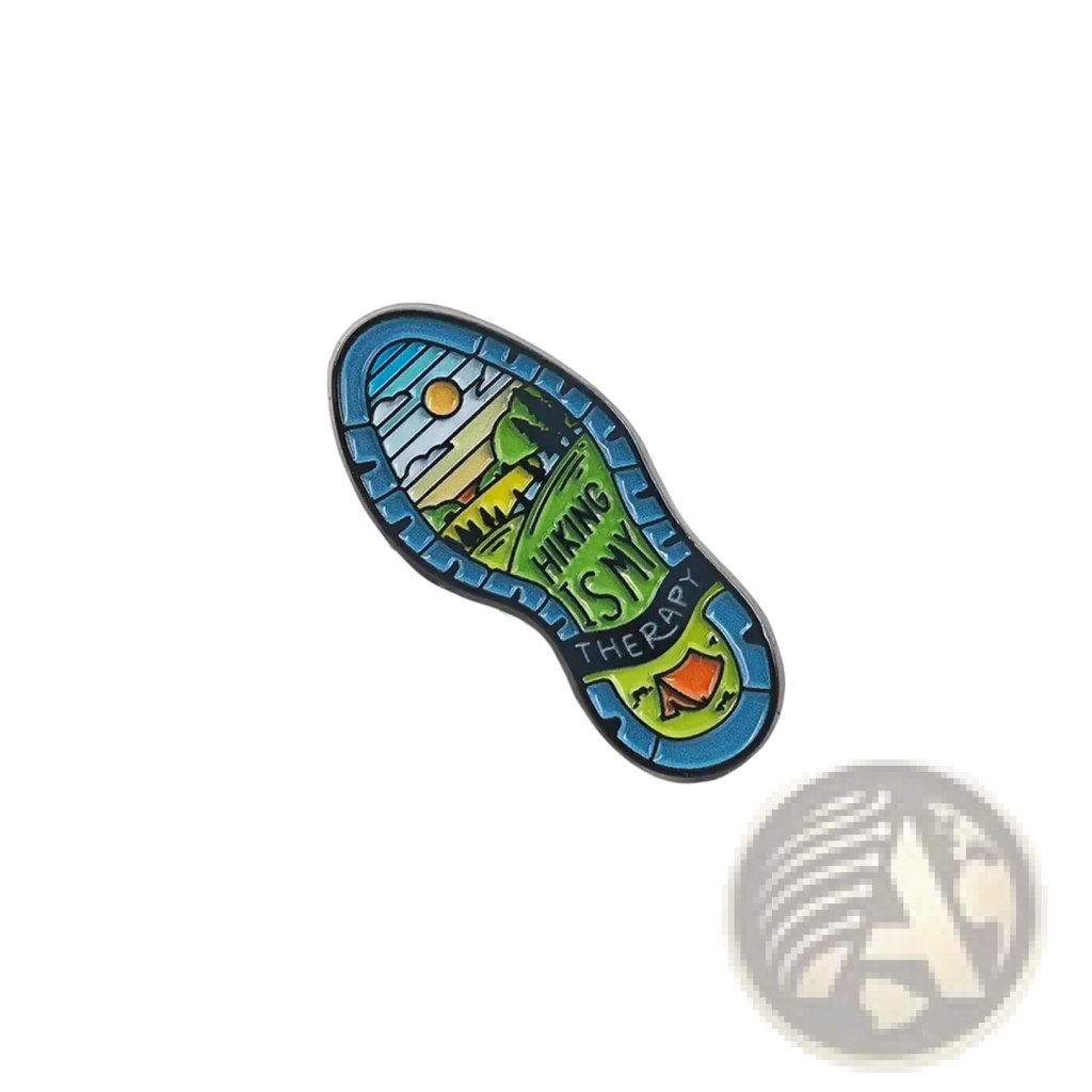 A colorful enamel hiking boot sole pin with a scenic landscape and hiking is my therapy text