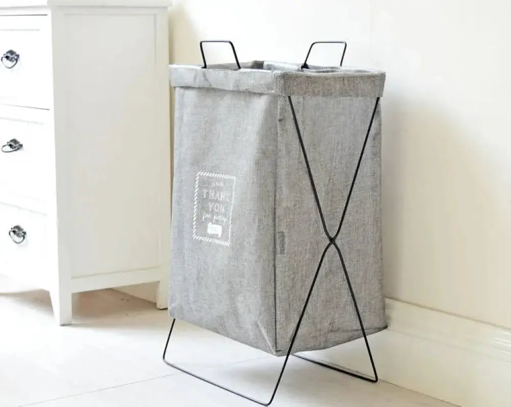 Gray fabric laundry hamper with black metal frame and handles featuring a white thank you label titled embroidered denim laundry basket with white metal frame