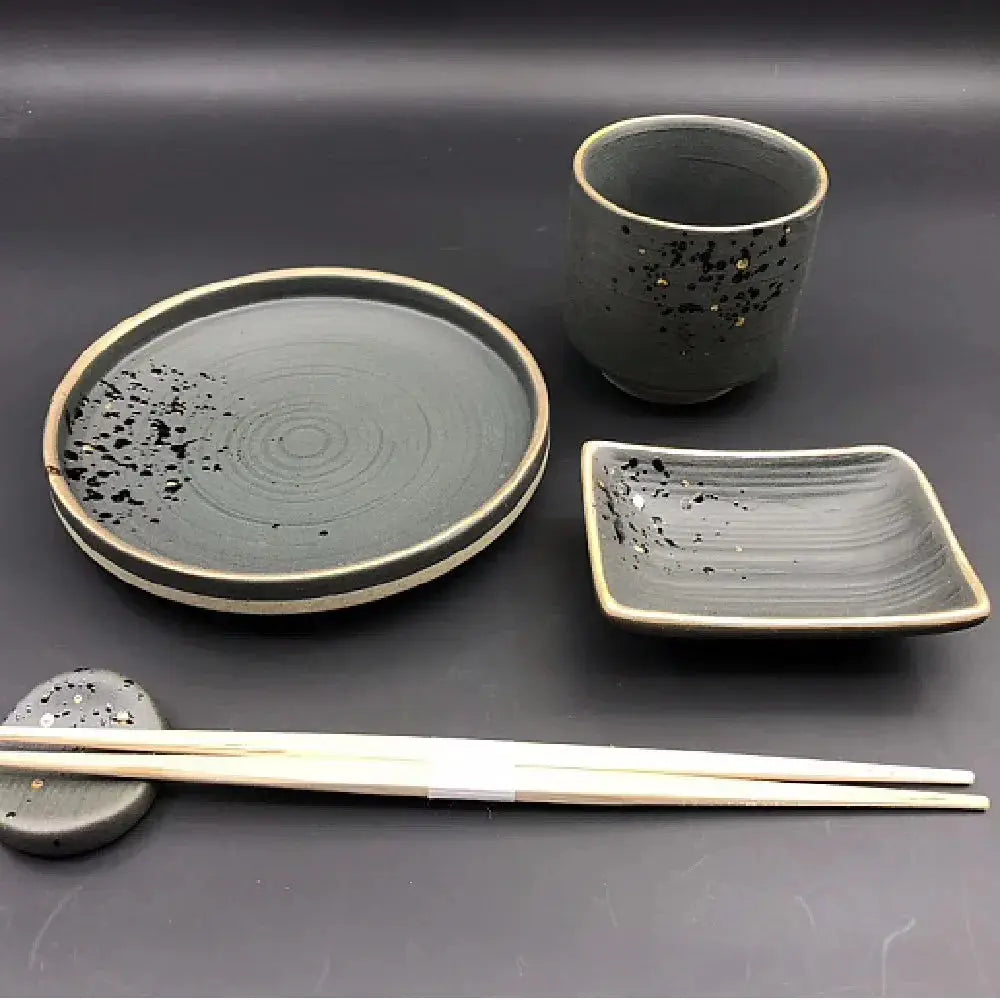 Minimalist Japanese ceramic speckled tableware set in dark gray with black speckles and beige rims including plate cup and chopstick rest
