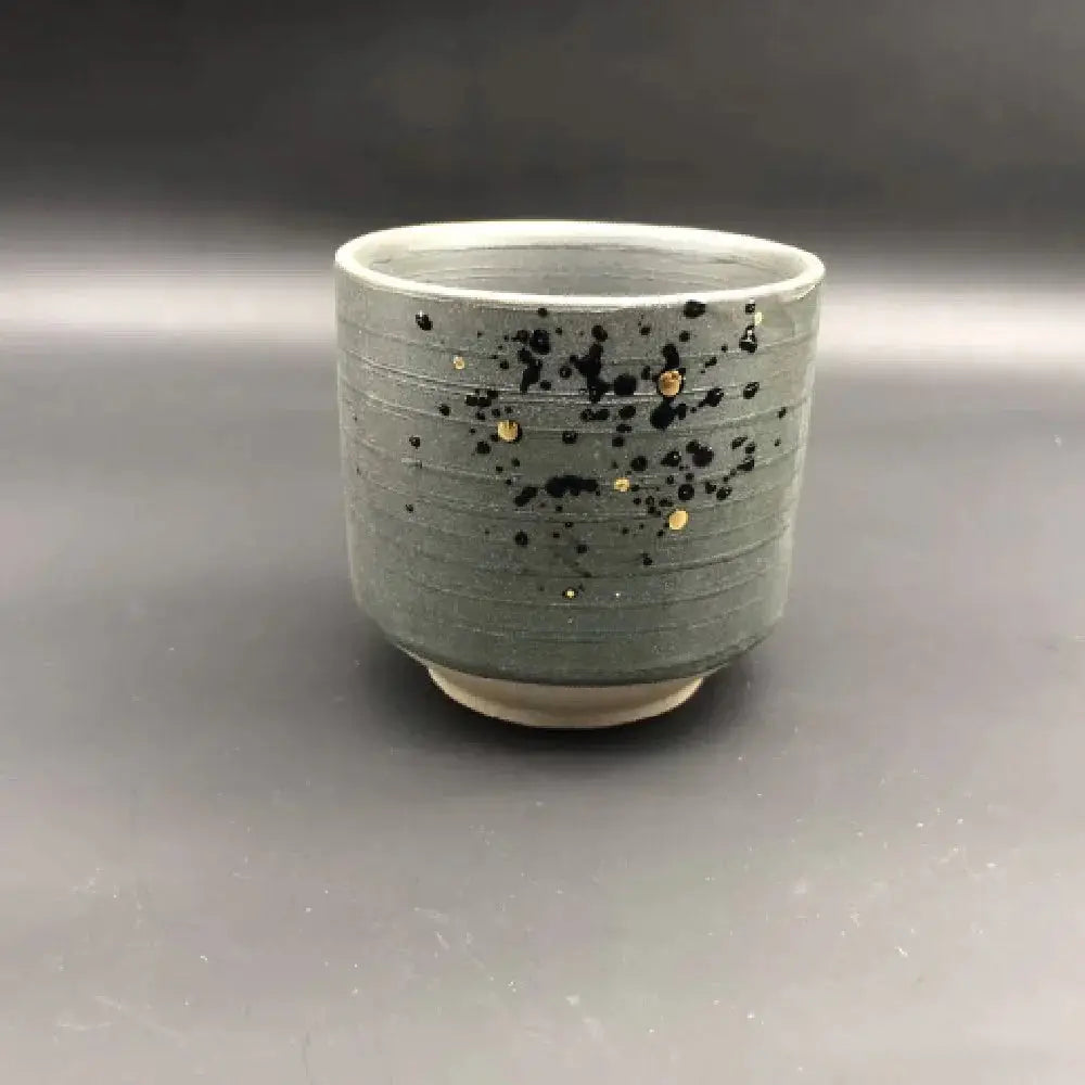 A gray minimalist Japanese ceramic tea cup with horizontal ridges and black and gold speckles