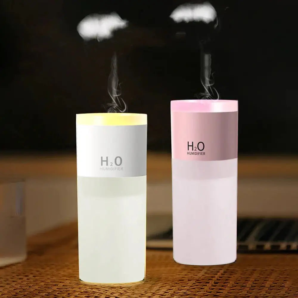 Two cylindrical portable USB LED mist humidifiers and aroma diffusers with white translucent and pinkish purple bodies emitting mist