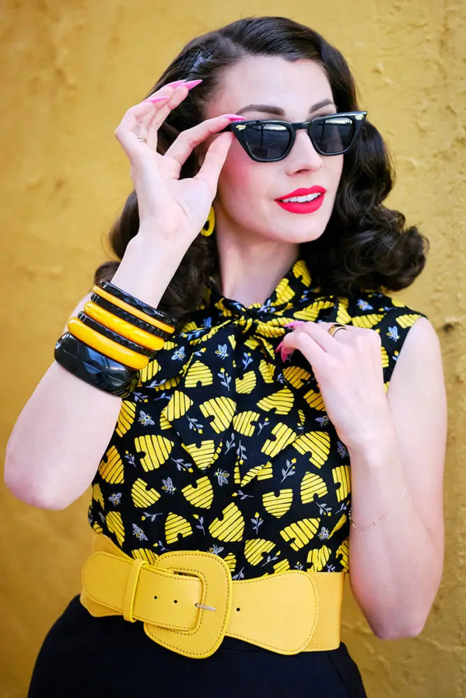 A woman wearing a honey hives vintage 1950s cotton bow top in black and yellow with a bold yellow belt