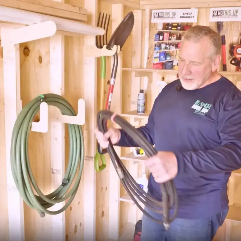 Black rubber garden hose coiled on a heavy duty wall mounted hose and extension cord organizer