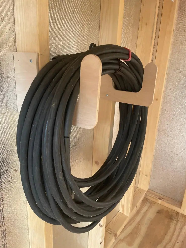 Heavy duty wall mounted hose and extension cord organizer holding a black coiled garden hose on a light wood hanger