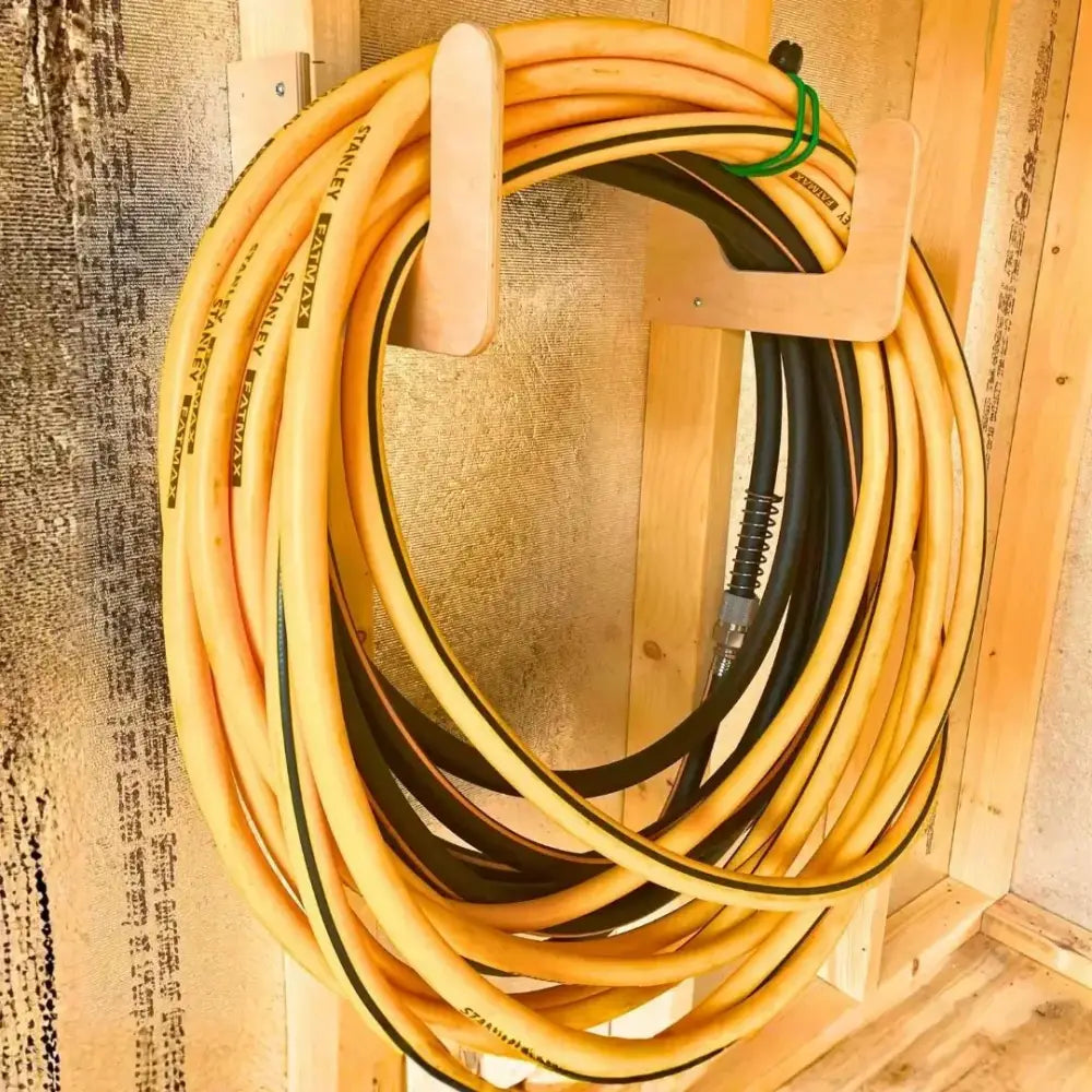 Heavy duty wall mounted hose and extension cord organizer holding a coiled yellow and black Stanley Fatmax air hose
