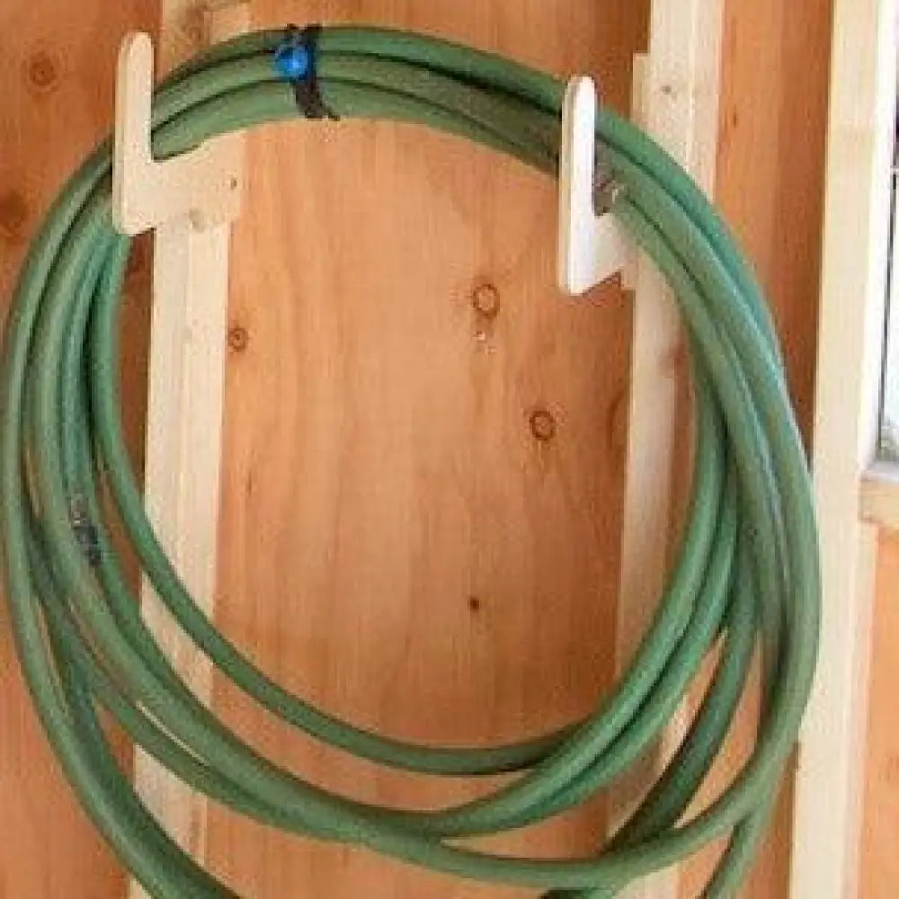 Heavy duty green garden hose coiled on a wooden wall mounted hose and extension cord organizer rack