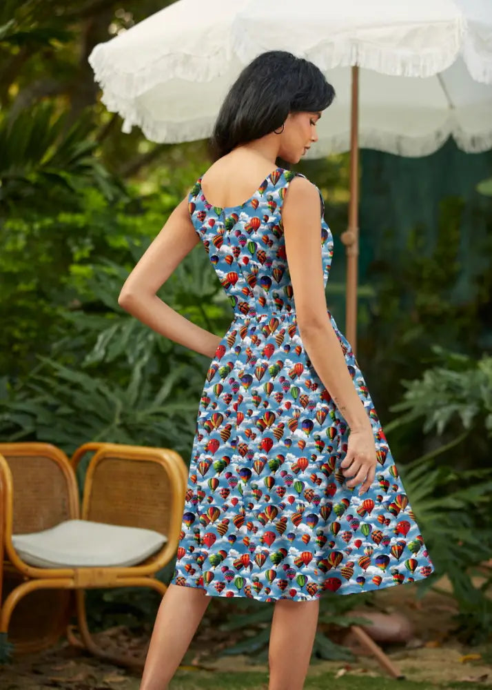 A woman wearing a vintage hot air balloon print cotton fit and flare sleeveless dress with a vibrant blue background