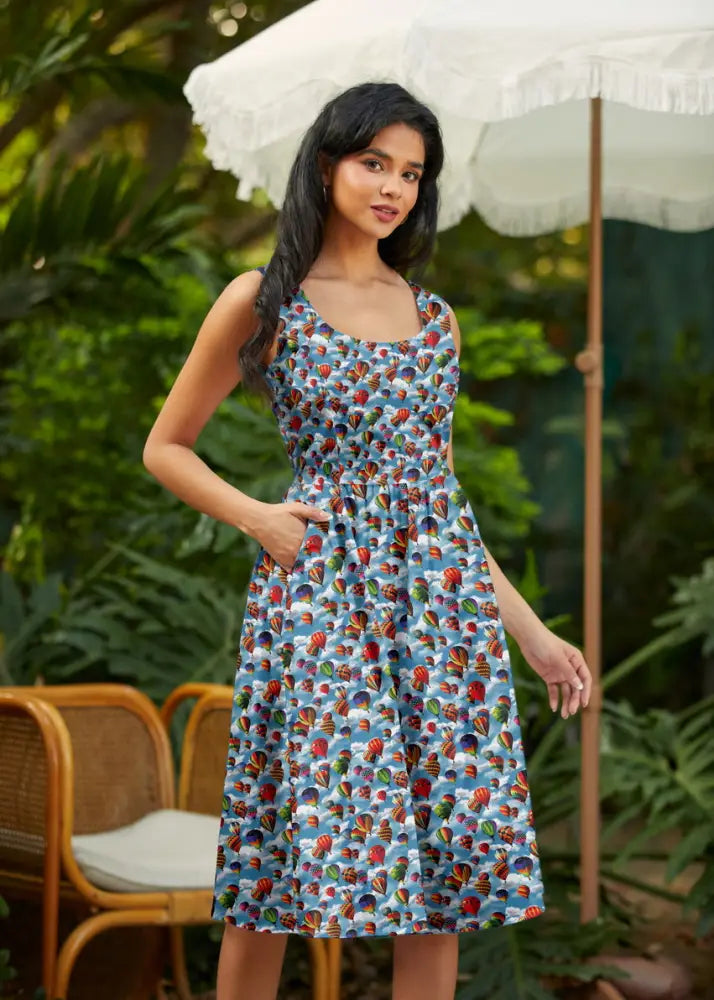 A sleeveless light blue cotton fit and flare dress with vintage colorful hot air balloon print and sky backdrop