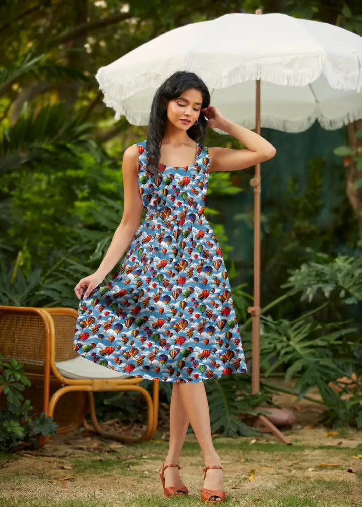 A woman wears a sleeveless vintage hot air balloon print cotton fit and flare dress with a vibrant blue base