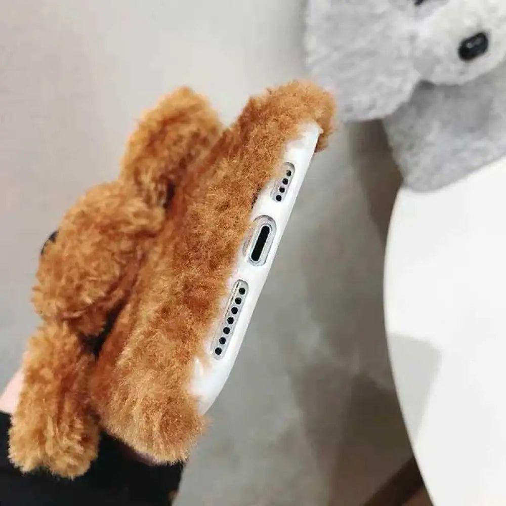 A plush tan teddy bear shaped phone case made of soft fuzzy material with rounded ears for phone protection