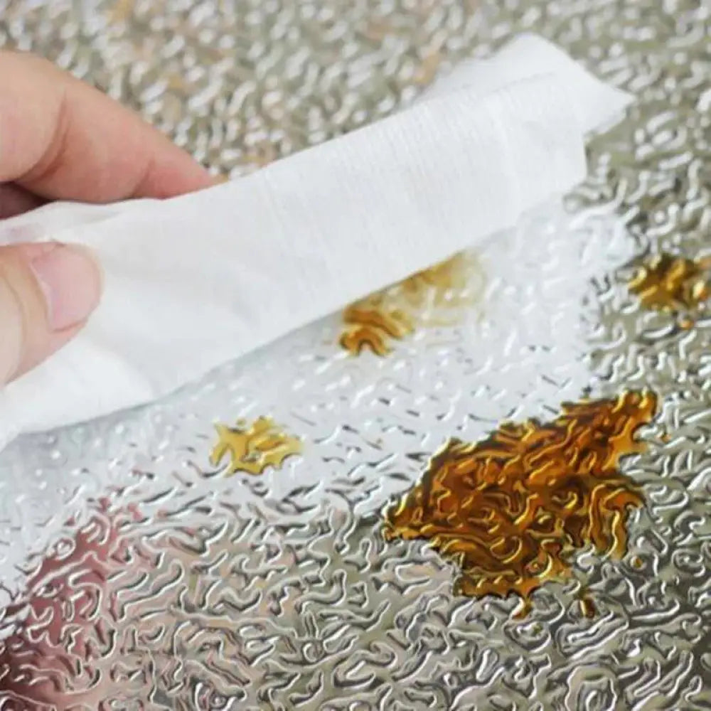 White paper towel wiping golden brown liquid on textured metallic surface in complete household kitchen utensil set for cooking