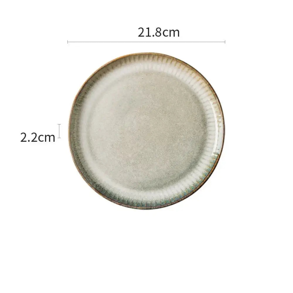 A round off-white ceramic plate with textured surface and fluted rim featuring a greenish-brown glaze from nordic ceramic dinnerware set