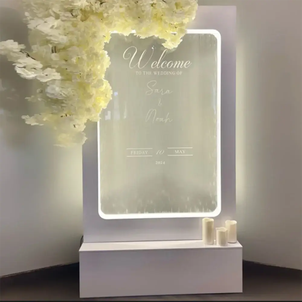 A sleek white acrylic illuminated wedding water fountain backdrop sign with elegant cursive engraving and glowing border
