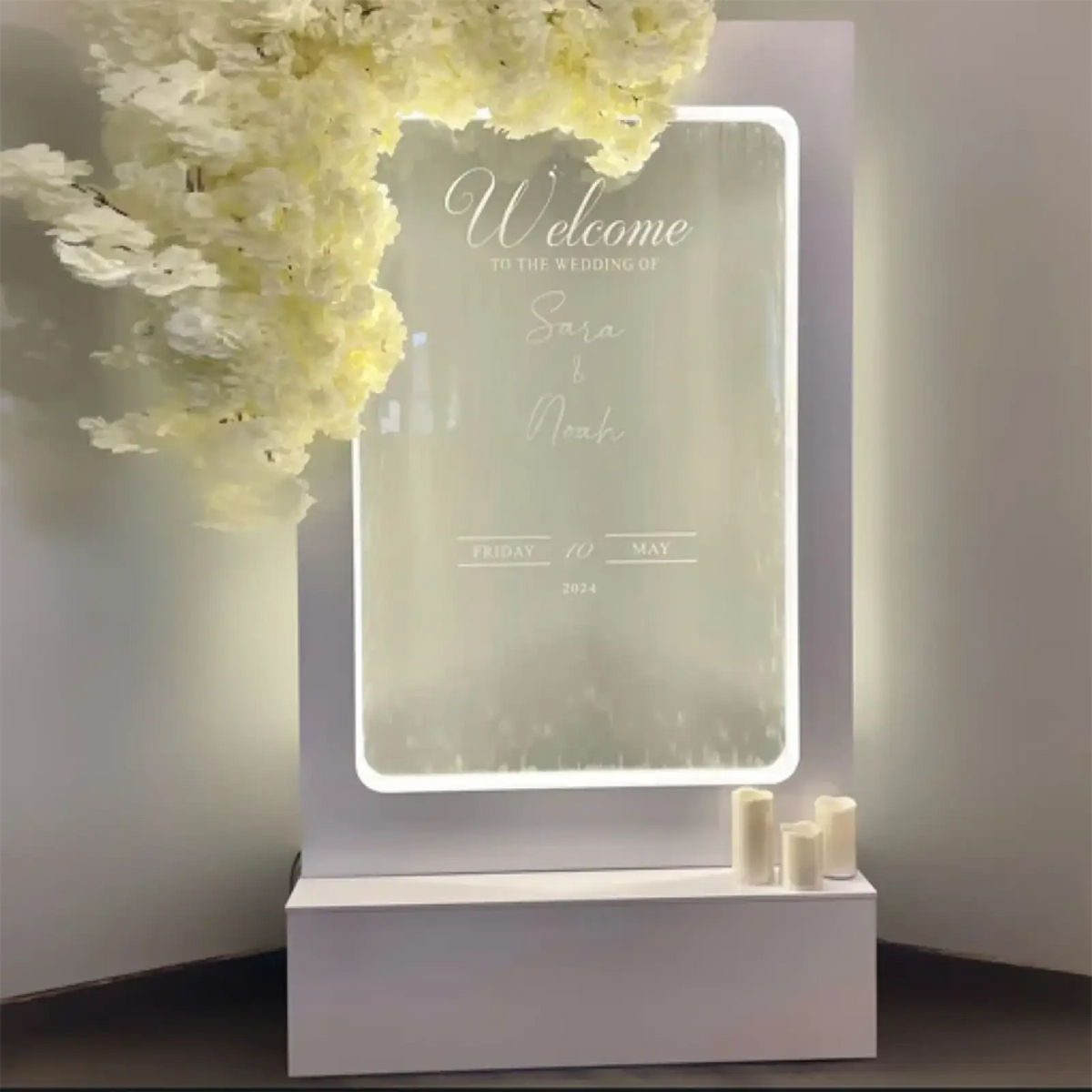 A sleek white acrylic illuminated wedding water fountain backdrop sign with elegant cursive engraving and glowing border