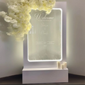 A sleek white acrylic illuminated wedding water fountain backdrop sign with elegant cursive engraving and glowing border