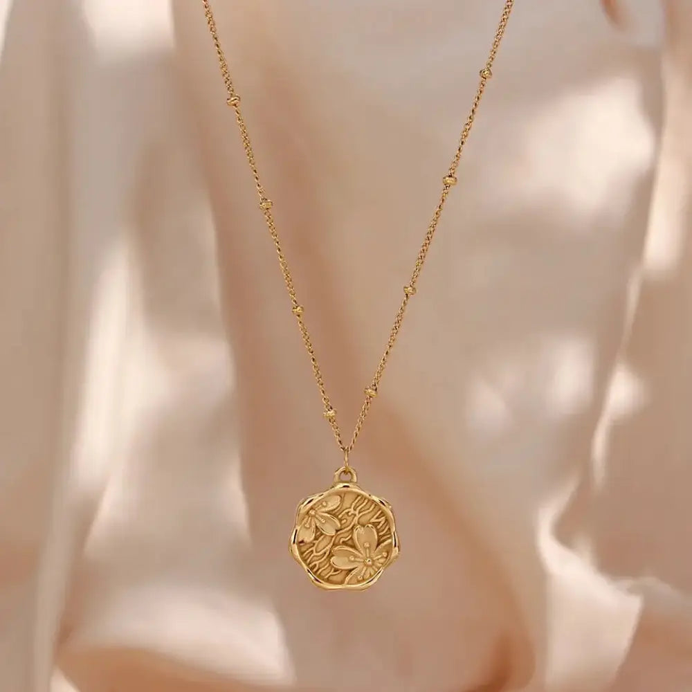 A delicate gold-toned floral pendant necklace with intricate engravings on a fine chain with small beads