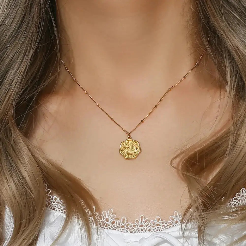Gold-toned coin-shaped engraved floral pendant necklace with intricate embossed design on delicate chain