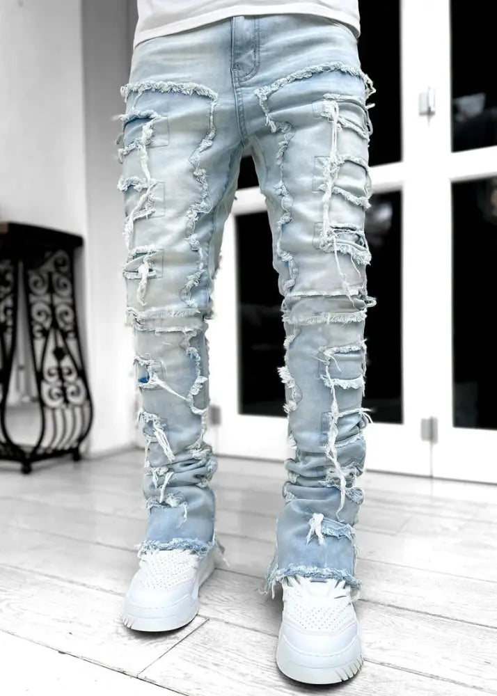 Men’s slim fit light-wash denim jeans with extensive frayed distressing and layered patchwork detailing