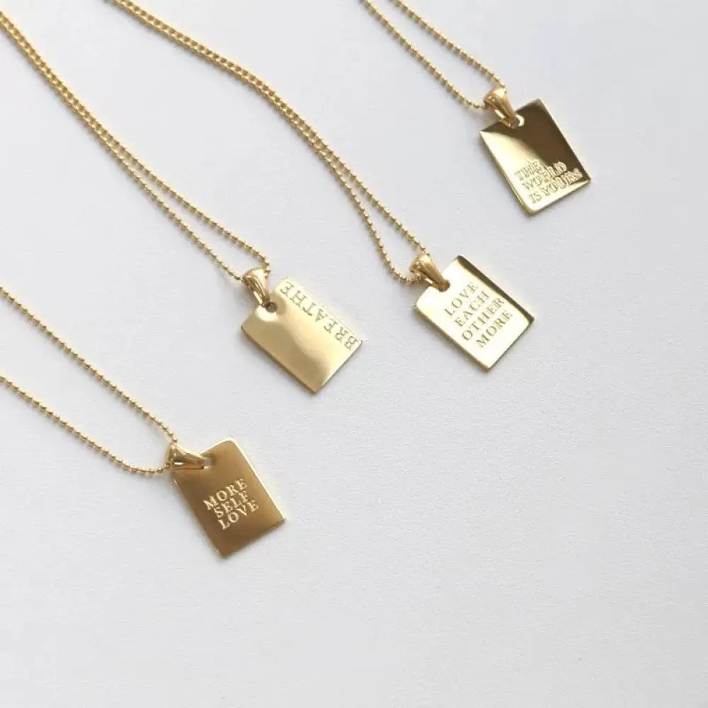 Gold-toned layered rectangular pendant necklace with engraved motivational phrases in a breathe tag design