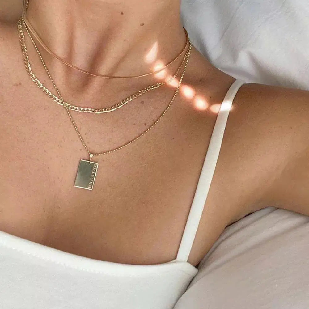 Gold layered breathe engraved tag necklace featuring gold toned layered chains with a rectangular pendant reading breathe