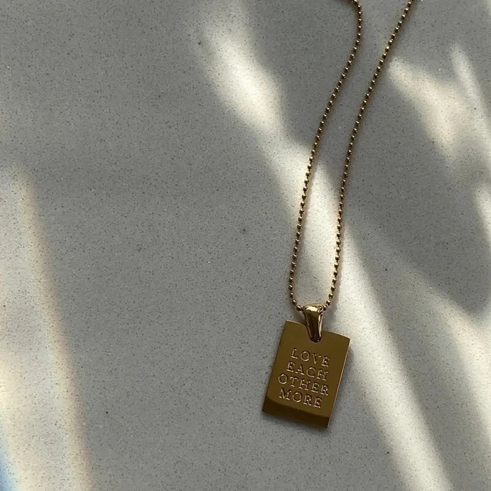 Gold layered rectangular pendant necklace in gold tone with engraved text love each other more on a delicate ball chain