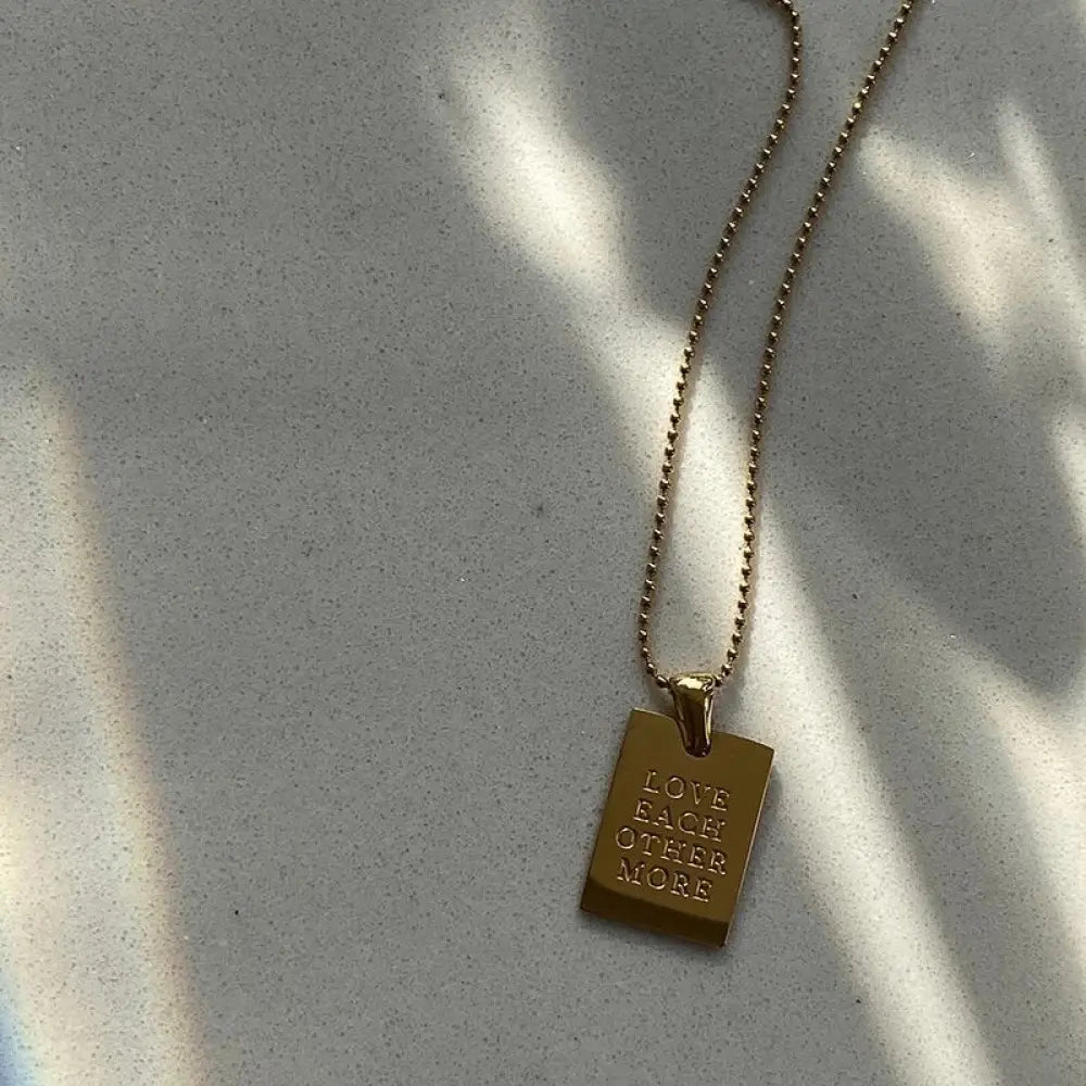 Gold layered rectangular pendant necklace in gold tone engraved with love each other more on a delicate ball chain