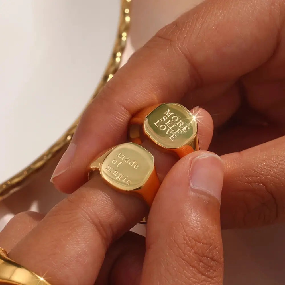 Engraved gold toned inspirational signet rings with polished metallic finish and orange-colored bands
