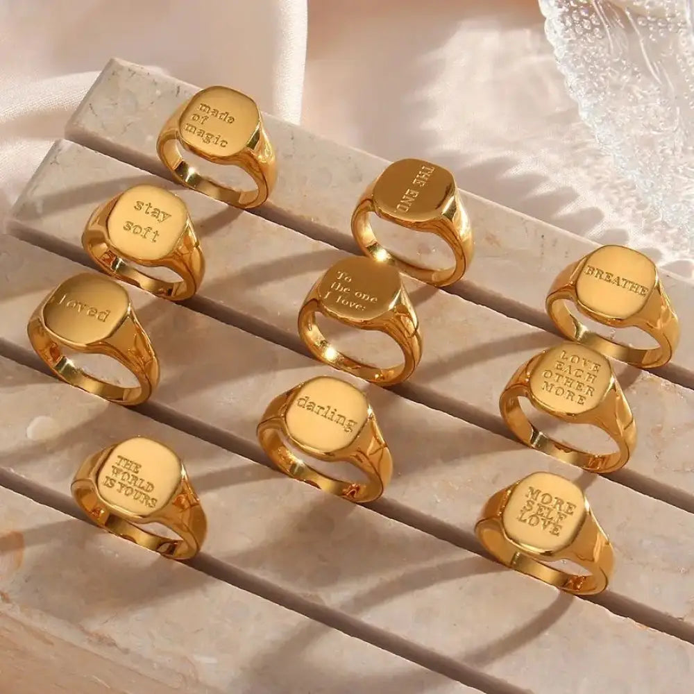 Gold toned signet rings with engraved inspirational phrases on flat rectangular faces for stylish motivation