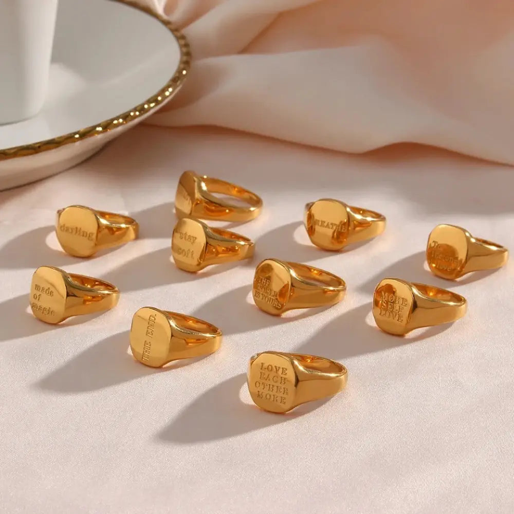 Engraved gold toned inspirational signet rings with polished metallic finish and phrases love each other more and made of magic