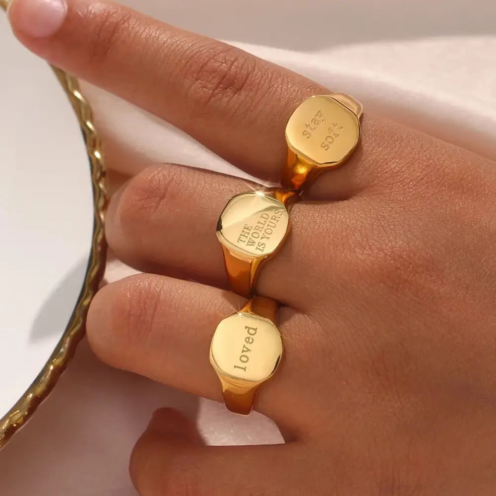 Engraved gold toned inspirational signet rings in gold with phrases like star soft the world is yours and loved on a hand