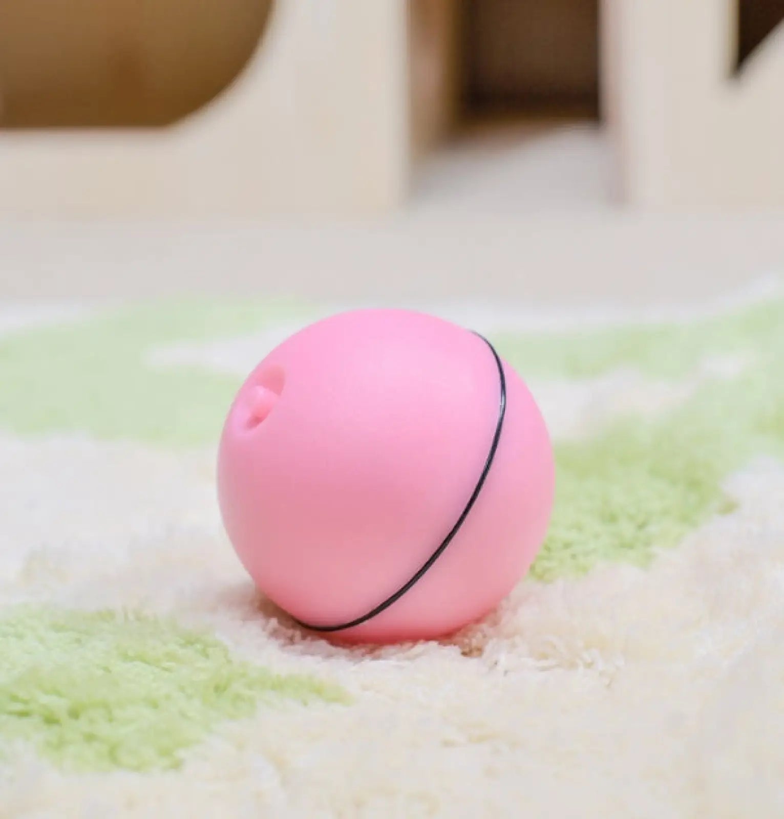 Interactive led cat toy ball in pink with a black elastic band and a small hole for catnip and feathers