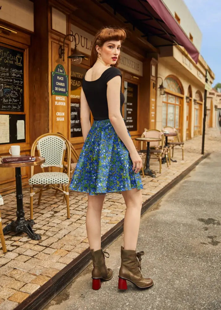 A woman wearing an irises floral print vintage skater skirt with elastic waist in vibrant blue paired with brown heeled boots