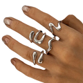 A set of five silver irregular geometric rings with fluid wavy and teardrop shapes worn on fingers for fashion