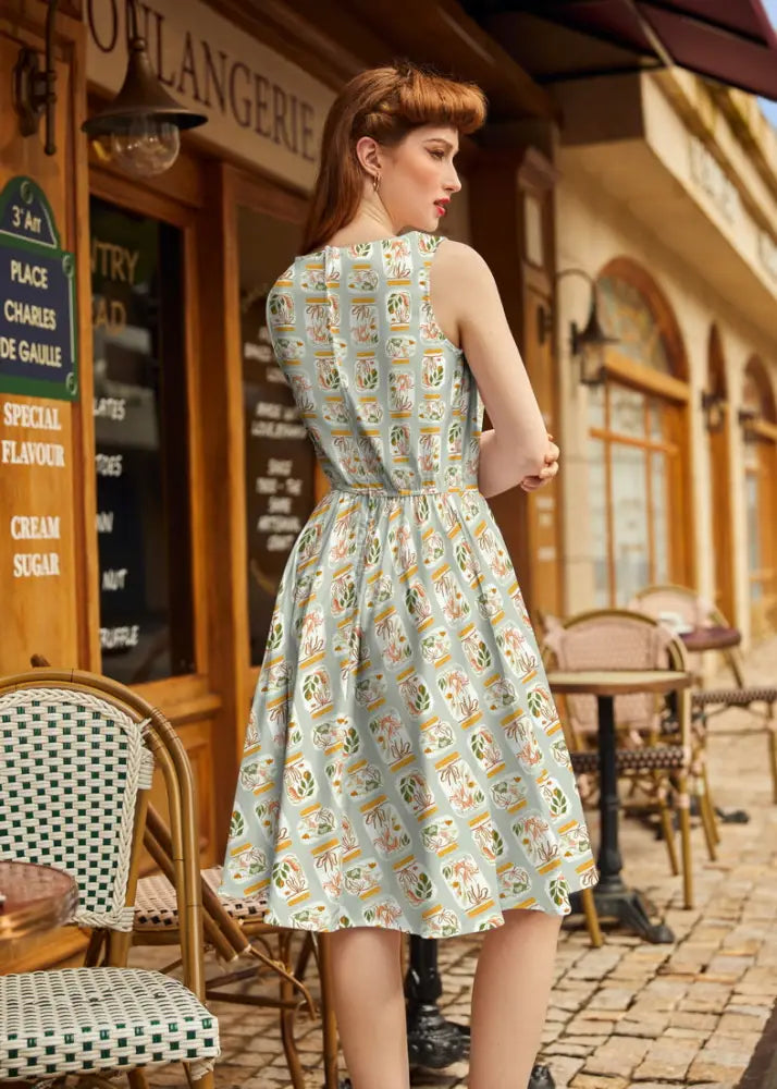 A light blue vintage 1950s cotton sleeveless dress with jars print, fitted bodice, flared skirt, gold accents, and pockets