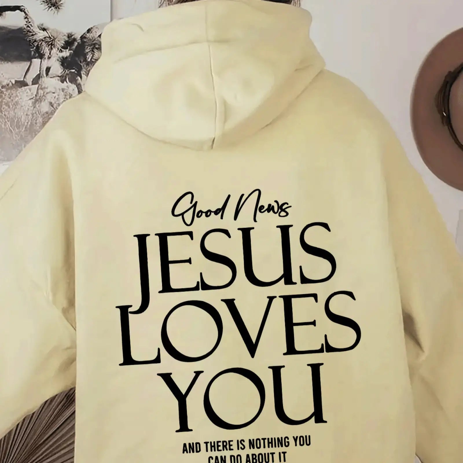 Back of cream-colored oversized streetwear hoodie with bold black good news jesus loves you text and kangaroo pocket