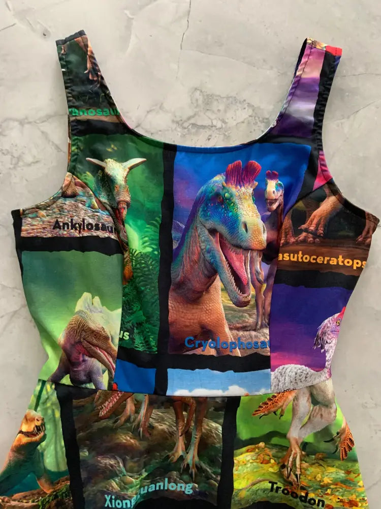 A vibrant sleeveless dinosaur-themed bodysuit with colorful cryolophosaurus and triceratops illustrations