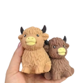 Two plush textured kawaii highland cow squishy stress relief toys in tan and brown with black horns and yellow snouts
