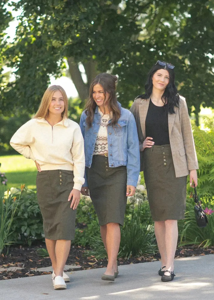 Three women walk in a park wearing kennedy olive button front midi denim skirts with button closures