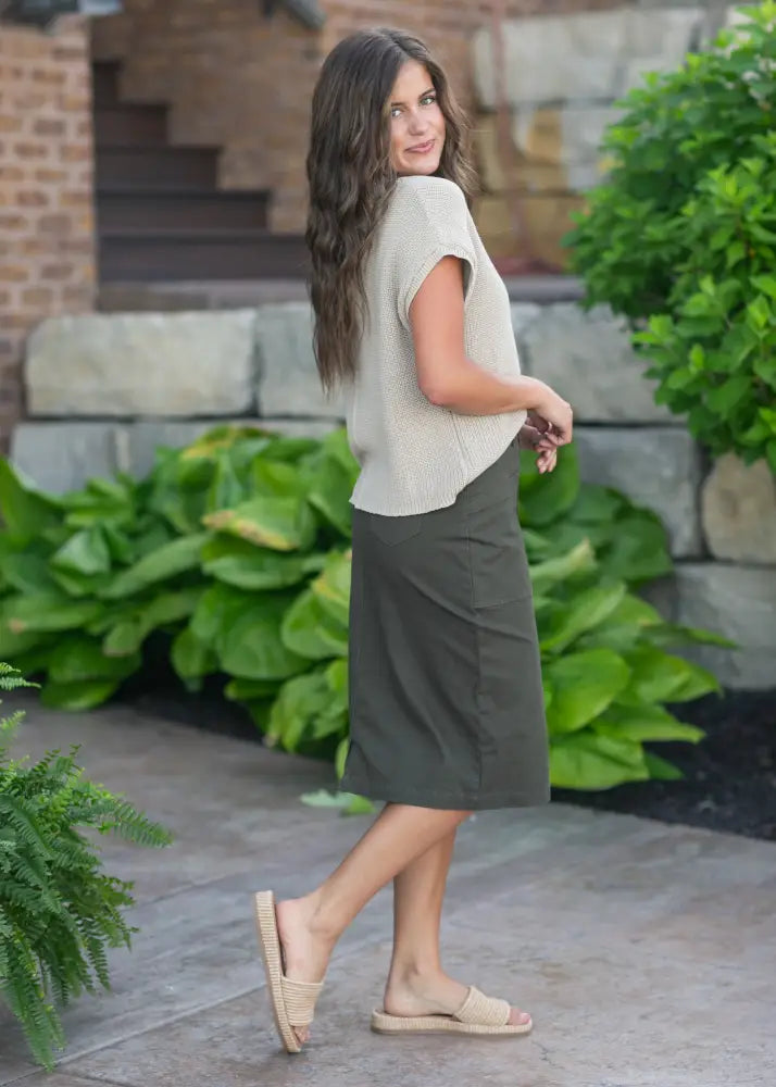 A woman wearing a kennedy olive button front midi denim skirt paired with a beige knit top and woven slide sandals
