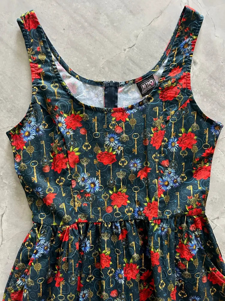 A dark navy sleeveless vintage fit and flare cotton dress with vibrant red roses blue flowers and gold keys pattern