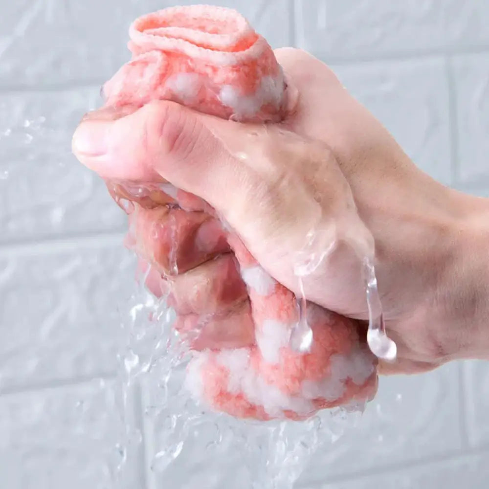 A pink and white striped coral fleece kitchen cleaning cloth being squeezed with water droplets falling